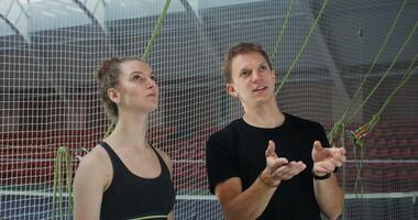 Young couple of European appearance, dressed in sportswear, discussing climbing a climbing wall, standing at the foot of the wall in a modern hall, close-up photo