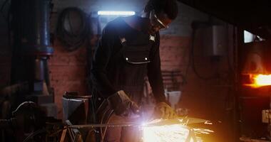 A man of African American appearance, dressed in work clothes and goggles with a concentrated look, uses a plasma cutter, cutting a sheet of iron, while working in a forge. 4k, red komodo - clothes photo