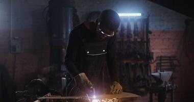 A man of African American appearance, dressed in work clothes and goggles with a concentrated look, uses a plasma cutter, cutting a sheet of iron, while working in a forge. 4k, red komodo - dressed photo
