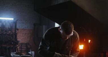 A young man of European appearance, dressed in work clothes and goggles, cuts a sheet of iron with a plasma cutter while working in a forge. 4k, red komodo - clothes photo