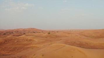 Drone view of a lifeless desert with sparse vegetation among red sand. Cars drive into a sandy mountain in the background - sparse photo