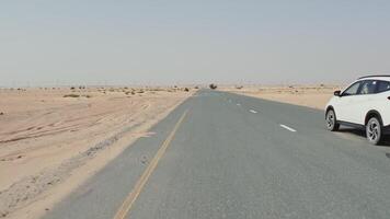 A drone view of a car driving along a road through a desert with sparse vegetation among the sands - sparse photo