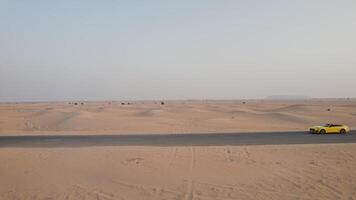 The drone flies parallel to a yellow car driving along the road among the desert sands photo
