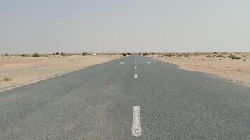 A drone view of a car driving along a road through a desert with sparse vegetation among the sands photo