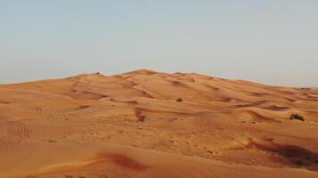Drone view of a lifeless desert with sparse vegetation among red sand. Cars are standing on a sandy mountain in the background photo