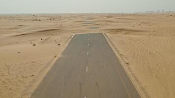 The drone flies over a modern paved road in the middle of a desert with sand dunes covering it photo