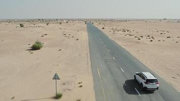 A drone view of a car driving along a road through a desert with sparse vegetation among the sands - desert photo