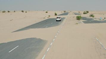 The car drives along an asphalt road covered with sand dunes in the desert, making its way through them. Drone view - covered photo