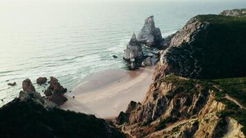The drone flies over the top of a grassy mountain overlooking the sea, with a sandy beach between the rocks photo