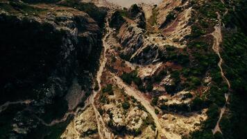 The drone flies from the top of a mountain overgrown with grass towards the sea, with a sandy beach between the rocks photo