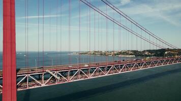 The drone flies near the red suspension bridge over the river, with cars passing on it - passing photo