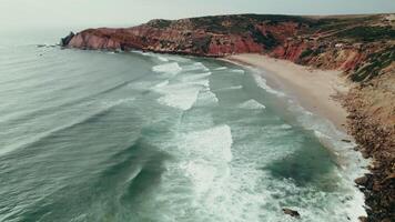Bird's-eye view of the seashore with a cliff covered with green grass at the top, a narrow strip of sandy beach at the foot of the mountain, drone photo