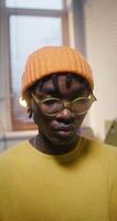 A man with glasses and a knitted hat is working sitting at a desk in the office, close-up of his focused face photo
