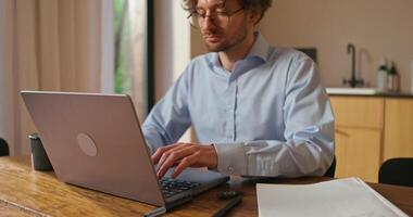 A man with glasses works from home. He uses a laptop and drinks coffee sitting at the kitchen table - drinks photo