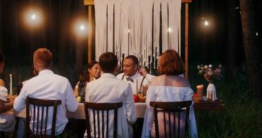 Guests smile and talk while sitting at a beautifully set festive table outdoors at night by candlelight - candlelight photo