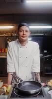 A man in a chef's uniform smiles while looking at the camera standing in the restaurant kitchen photo