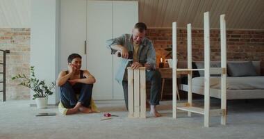 A woman is talking on a mobile phone sitting on the floor next to a man assembling a rack with a screwdriver, they are talking - sitting photo