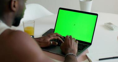 A man uses a laptop with a green screen sitting at a table at home, close-up of his hands, an unrecognizable person. Daylight - sitting photo