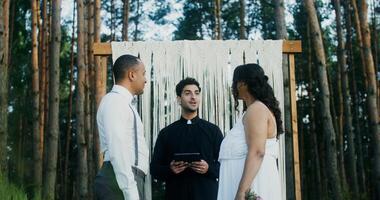 The bride and groom kiss at the wedding standing in front of the altar. Wedding in the forest with a priest - Wedding photo