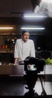 A man in a chef's uniform records the cooking process on , standing near a frying pan in the kitchen of a restaurant photo
