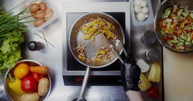 A woman in disposable black gloves mixes mushrooms with pepper in a frying pan with tongs, top view, close photo