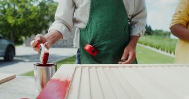 A man in an apron and a boy paint the door with red paint while standing in the backyard. Close-up of hands, no face - standing photo