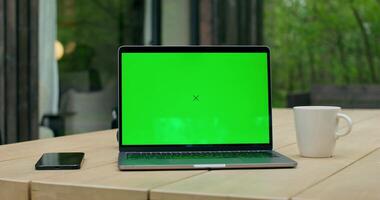 An open laptop with a green screen is on a table on the terrace of a stylish cottage. photo