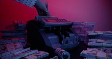 A man's hand with a ring inserts a stack of hundred-dollar bills into the counting machine and it starts counting. Bundles of money are lying around on the table photo