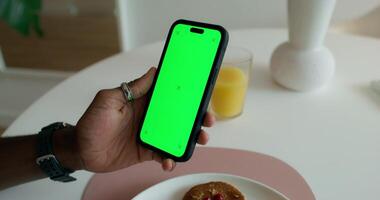 A man uses a mobile phone with a green screen during breakfast at home. Close-up of his hand, an unrecognizable person - breakfast photo