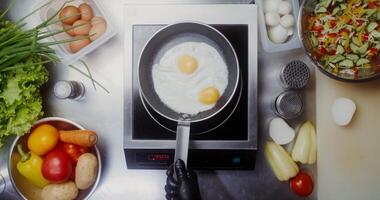 A woman in disposable black gloves adds seasonings to eggs frying in a frying pan, close photo
