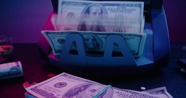 The calculating machine counts hundred dollar bills. Bundles of money are on the table next to a gun, a lighter, an ashtray and other objects - Bundles photo