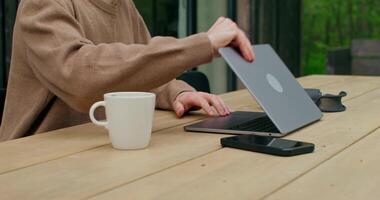 A man is typing on a laptop sitting at a table on the terrace of the cottage. Close-up of his hands, an unrecognizable person photo