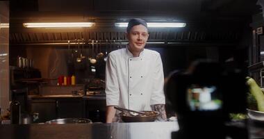 A man in a chef's uniform records the cooking process on , standing near a frying pan in the kitchen of a restaurant - frying photo