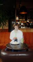 A woman in casual clothes uses a mobile phone and drinks a cocktail while having breakfast in a cafe photo