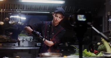 A woman in a chef's uniform talking and smiling recording the cooking process in the restaurant kitchen on camera - process photo