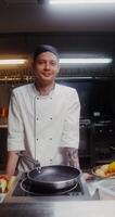 A man in a chef's uniform smiles while looking at the camera standing in the restaurant kitchen - looking photo