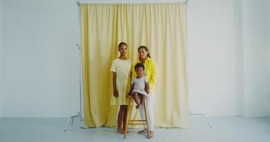 A mother with two children smiles while looking at the camera posing in the studio. The baby is sitting on a high chair - smiles photo