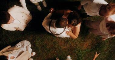 Elegant guests smile and dance leading a round dance around the bride and groom at an outdoor party at night, top view - leading photo