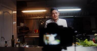 A man in a chef's uniform records the cooking process on , standing near a frying pan in the kitchen of a restaurant - standing photo