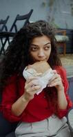 A young woman in casual clothes eats a burger and drinks a mojito while sitting in a cafe - drinks photo