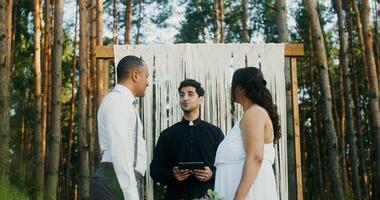 The bride and groom kiss at the wedding standing in front of the altar. Wedding in the forest with a priest photo