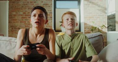 Mom and son of European appearance smile playing games using joysticks sitting on the couch in a stylish home interior - sitting photo