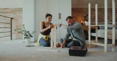 A man and a woman assemble a shelving at home, they use a screwdriver, talk and smile sitting on the floor - sitting photo