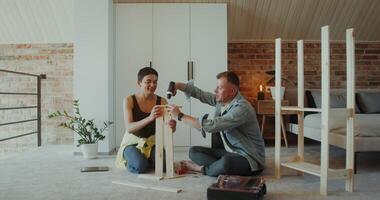 A man and a woman assemble a shelving at home, they use a screwdriver, talk and smile sitting on the floor photo