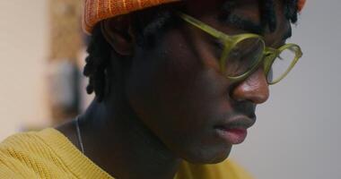 A man with glasses and a knitted hat is working sitting at a desk in the office, close-up of his focused face - working photo