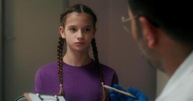 The doctor talks to the girl patient, finding out the symptoms of the disease and writes in a notebook, sitting in the medical office at the clinic - symptoms photo