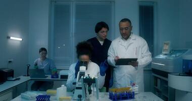 A group of laboratory technicians perform a blood test in the laboratory. A man and a woman use a tablet standing near a laboratory assistant's desk with a microscope - laboratory photo