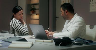The doctor listens to the patient's complaints sitting in front of an open laptop at the table and writes in a notebook. Medical appointment at the clinic photo