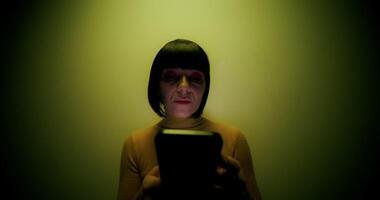 A woman in a wig uses a mobile phone, leaning against the wall in the orange backlight in the studio - backlight photo