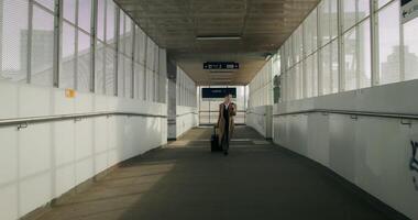 A woman in formal clothes and a coat uses a mobile phone walking along the corridor of the railway station - mobile photo